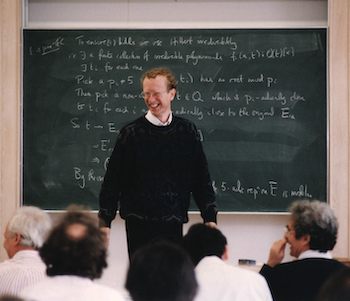 Andrew Wiles, smiling, standing in front of the black board covered with with work, announcing his proof of Fermat's Last Theorem on 23 June 1993 (Image courtesy of the INI)
