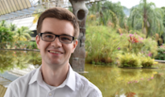 Jack Thorne, smiling, sitting in front of a pond and tropical garden