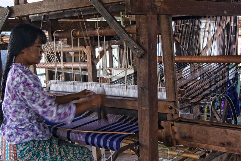 Woman in Myanmar sitting at loom weaving a striped purple fabric.